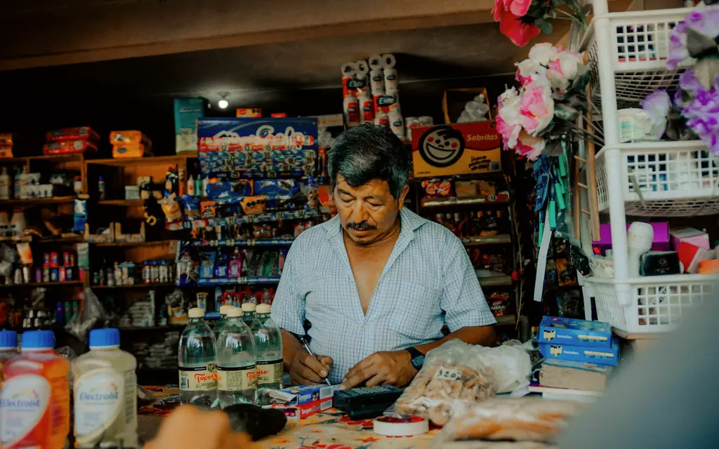 Un comerciante atiende en el mostrador de su tienda, rodeado de mercancía.