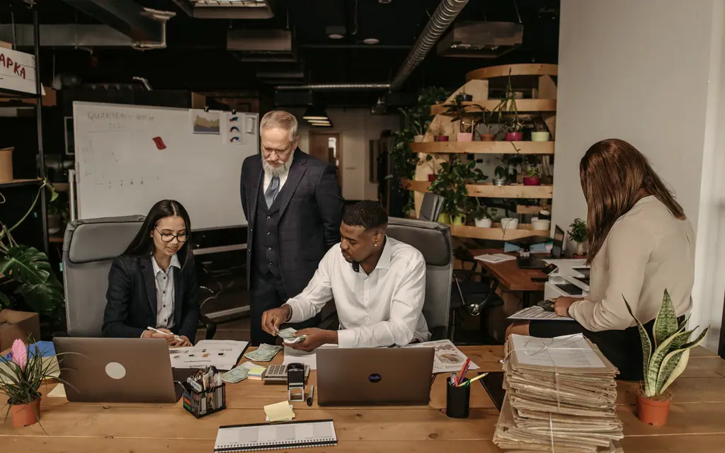Un equipo de oficina trabaja con computadoras y papeles en una mesa larga.